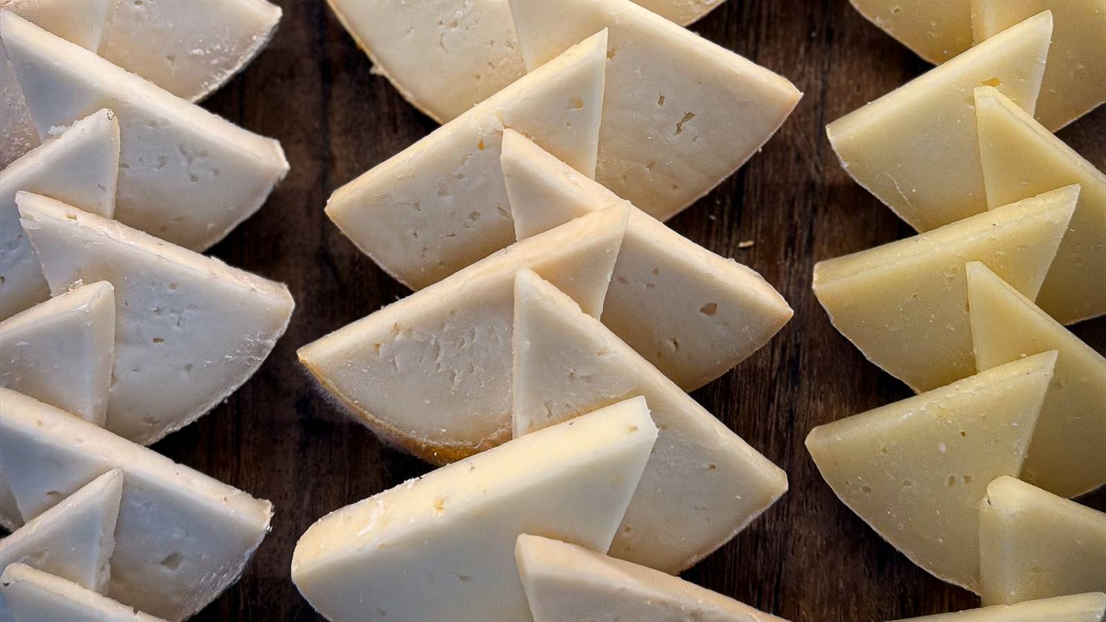 Cut wedges of hard cheese arranged in rows on a dark wooden surface