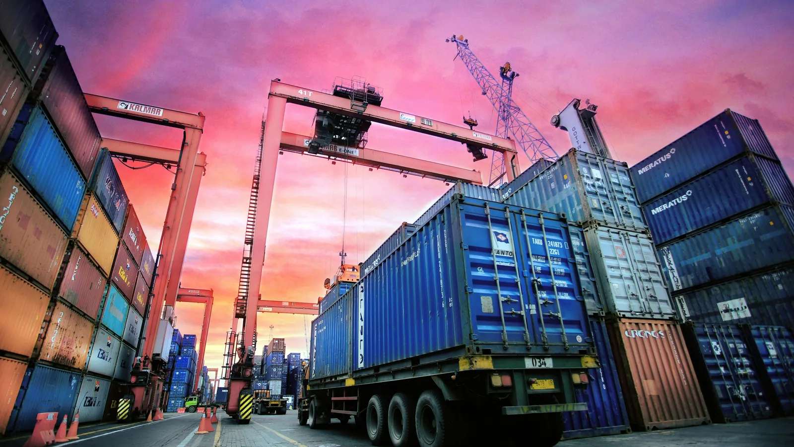 Shipping containers stacked at a busy UK port at sunset, carrying Italian food imports